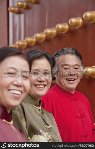 Group of mature people in traditional clothes standing next to traditional Chinese door, portrait