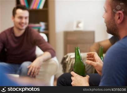 Group of men sitting in lounge holding beer bottles chatting