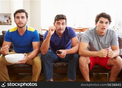 Group Of Men Sitting On Sofa Watching Sport Together