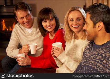 Group Of Middle Aged Couples Sitting On Sofa With Hot Drinks Talking