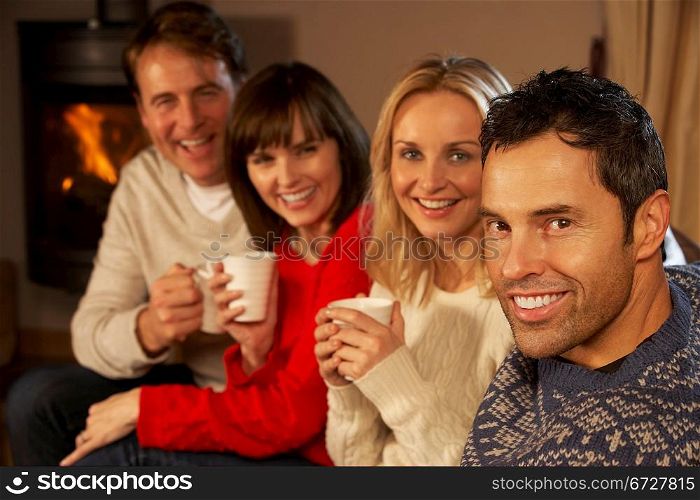 Group Of Middle Aged Couples Sitting On Sofa With Hot Drinks Talking