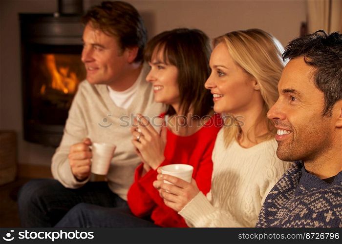 Group Of Middle Aged Couples Sitting On Sofa With Hot Drinks Watching TV