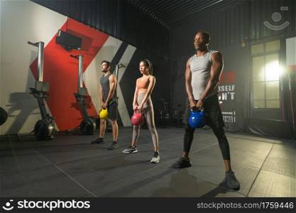 Group of multi ethnic people holding weight kettle bell twist, cardio. Strength training workout at gym fitness center club. Exercise indoor with sport equipment. People lifestyle recreation. Team