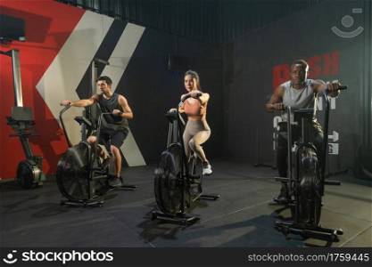 Group of multi ethnic people riding spinning bike or bicycle, Muscle strength training workout at gym fitness center club. Exercise with sport equipment. People lifestyle recreation. Strong team