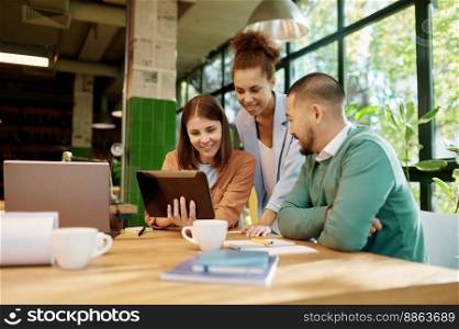 Group of multiracial business people coworker using digital tablet looking at screen. Idea of teamwork. Young smiling men and women at open space workspace. Multiracial office coworker team using digital tablet
