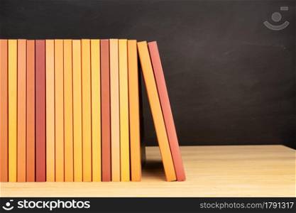Group of orange books on wooden table or shelves and blackboard at background. Copy space