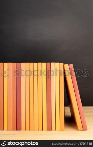 Group of orange books on wooden table or shelves and blackboard at background. Copy space