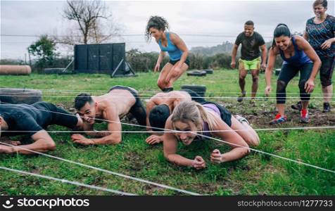 Group of participants in an obstacle course crawling under electrified cables. Participants in an obstacle course crawling