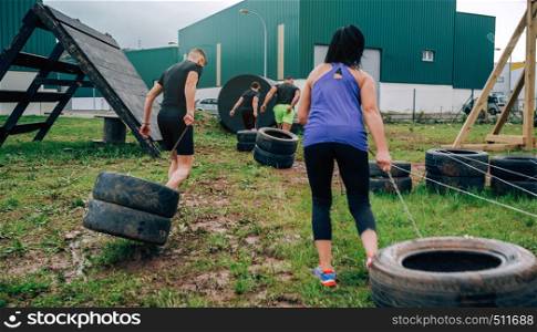 Group of participants in an obstacle course dragging wheels seen from behind. Participants in an obstacle course dragging wheels