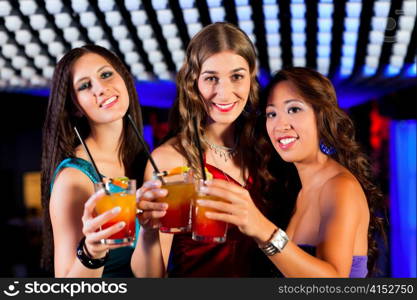 Group of party people with cocktails in a bar or club having fun; one woman is looking into the camera