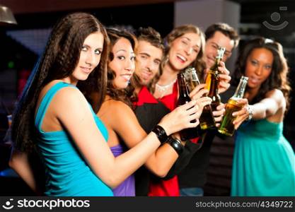 Group of party people with cocktails in a bar or club having fun; one woman is looking into the camera