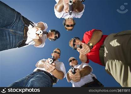 Group of people aiming guns in circle, low angle view