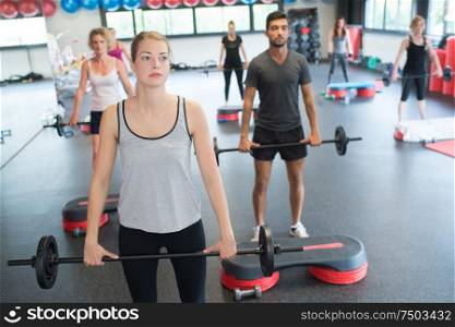 group of people exercising with barbell bars in gym