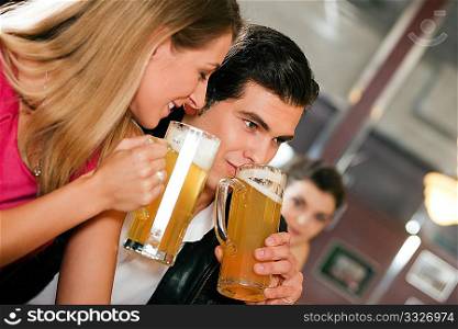 Group of people in a bar or restaurant drinking beer, one couple flirting very obviously having a lot of fun