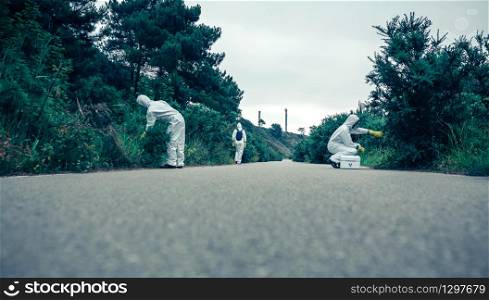 Group of people in bacteriological protection suits looking for samples on an empty road