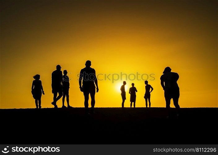 Group of people in silhouette walking towards the falling sun. People in silhoutte  in an orange background