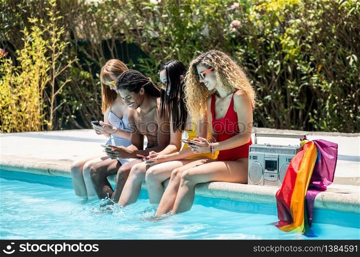 group of people of different ethnicities in swimsuits looking at the mobile phone at the edge of a pool