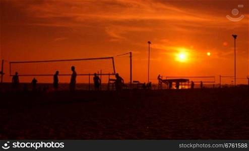 Group of people playing volleyball on a public beach at sunset