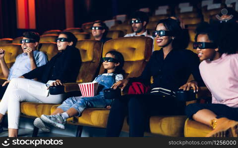 Group of people watch movie with 3D glasses in cinema theater with interest looking at the screen, exciting and eating popcorn