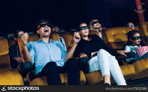 Group of people watch movie with 3D glasses in cinema theater with interest looking at the screen, exciting and eating popcorn