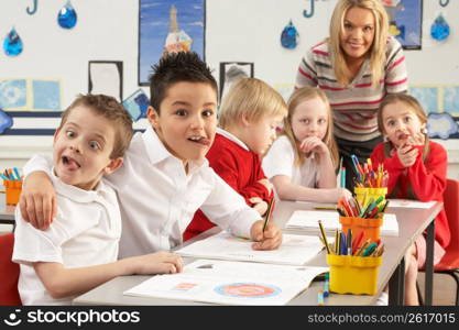 Group Of Primary Schoolchildren And Teacher Working At Desks In Classroom