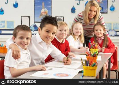 Group Of Primary Schoolchildren And Teacher Working At Desks In Classroom