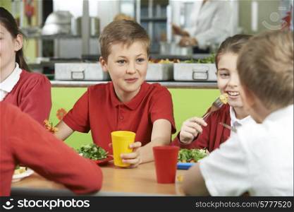 Group Of Pupils Sitting At Table In School Cafeteria Eating Meal