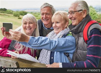 Group Of Senior Friends Hiking In Countryside Standing By Gate And Taking Selfie On Mobile Phone