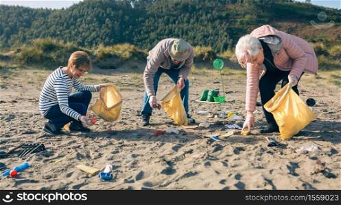 Group of senior volunteers picking up trash on the beach. Senior volunteers cleaning the beach