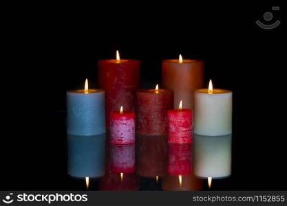 Group of several colored lit candles and its reflection on a glass table on a dark background. Spiritualism concept.. Group of colored lit candles with reflection