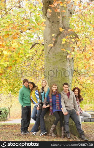 Group Of Six Teenage Friends Leaning Against Tree In Autumn Park