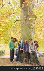 Group Of Six Teenage Friends Leaning Against Tree In Autumn Park