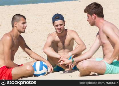 group of smiling male friends sitting on the beach