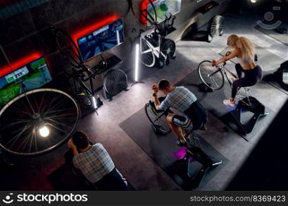 Group of sports people riding stationary bike exercise machine at gym. Fitness training indoor. Overhead view. Group of sports people riding stationary bike at gym
