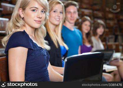 Group of students sitting in a row with laptop and book at seminar hall