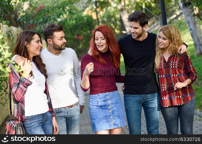 Group of students together outdoors in urban background. Women and men walking in the street wearing casual clothes.