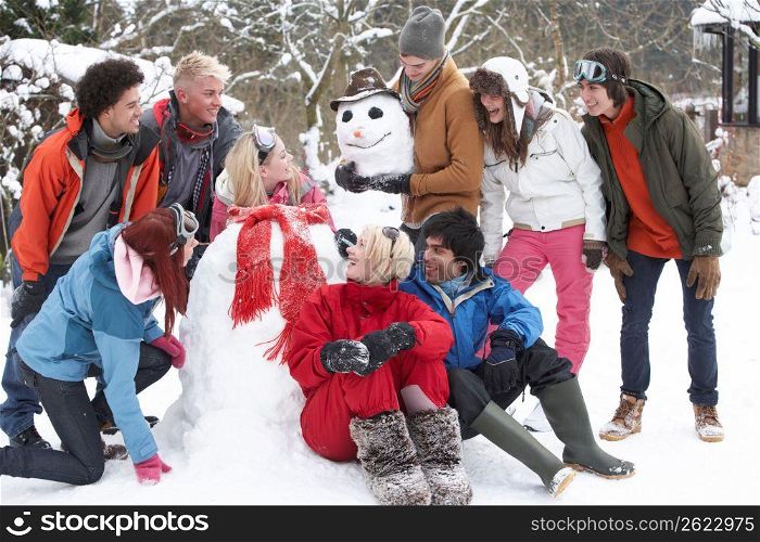 Group Of Teenage Friends Building Snowman In Garden