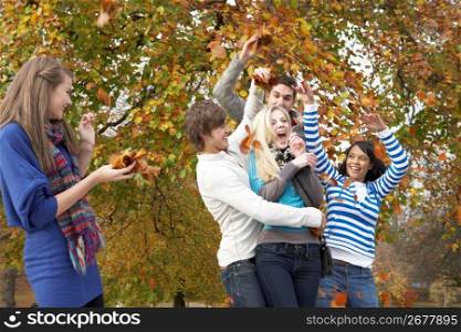 Group Of Teenage Friends Throwing Leaves In Autumn Landscape
