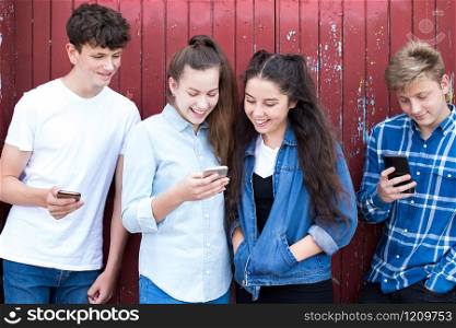 Group Of Teenage Froends Looking At Mobile Phones In Urban Setting