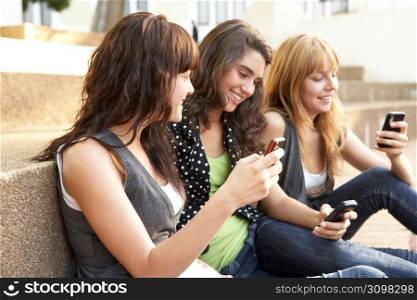 Group Of Teenage Students Sitting Outside On College Steps Using Mobile Phone