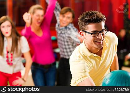 Group of three friends in a bowling alley having fun, two of them cheering the one in charge to throw the bowling ball