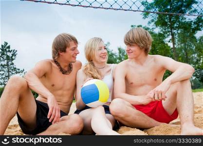 Group of three friends - one woman and two men - playing beach volleyball, the day is not overly sunny but they do not care and have fun nevertheless