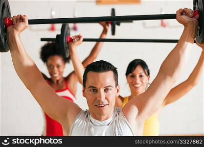 Group of three people exercising using barbells in the gym to gain strength and fitness