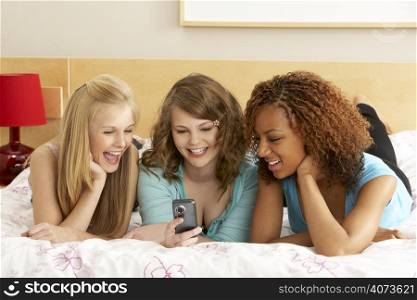 Group Of Three Teenage Girls Using Mobile Phone In Bedroom