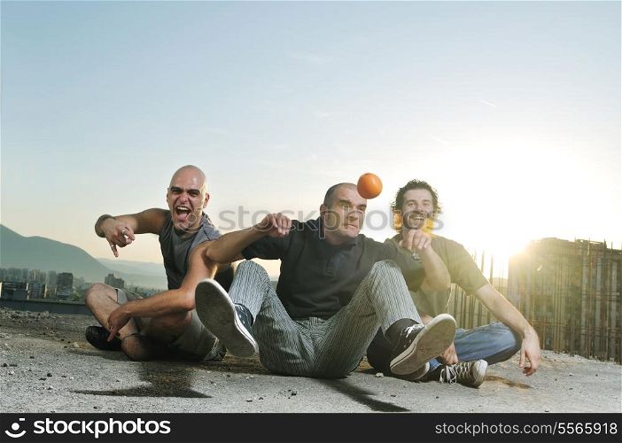 group of three young man outdoor in urban scene playing and have fun with orange fruit at sunsetgroup of three young man outdoor in urban scene playing and have fun with orange fruit at sunset
