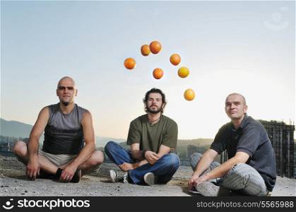 group of three young man outdoor in urban scene playing and have fun with orange fruit at sunsetgroup of three young man outdoor in urban scene playing and have fun with orange fruit at sunset