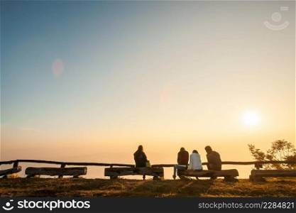 Group of tourist relaxing on logs on mountain peak under sun shining, winter season. Light blue sky and mountains backgrounds. Si Nan National Park. Copy space. Vacation time.