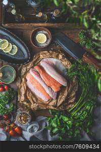 Group of various colorful fish fillets on eco friendly paper on rustic kitchen table background with fresh organic ingredients for tasty home cooking. Top view. Still life. Healthy homemade cuisine