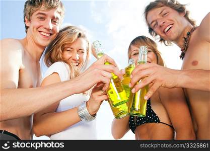 Group of very beautiful people celebrating on the beach in the summer of their lives - focus on bottles