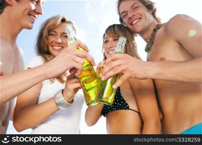 Group of very beautiful people celebrating on the beach in the summer of their lives - focus on bottles